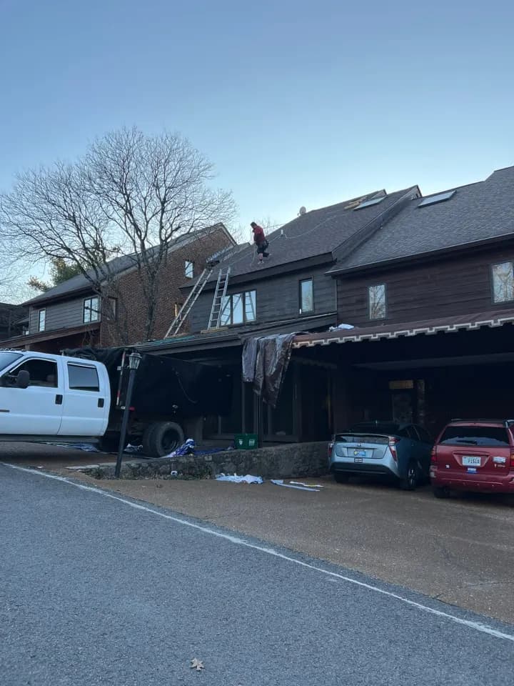 Mobley Brothers crew member on the roof of a two-story home during a new roof installation in Nashville, with a work truck and dump trailer in the driveway