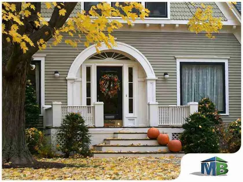 Front entry of a green-sided house with autumn leaves and pumpkins