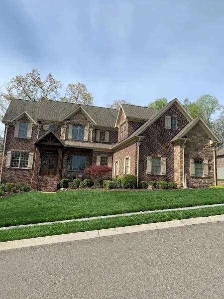 A large two-story brick and stone home with a gray roof, landscaped front yard, and paved driveway
