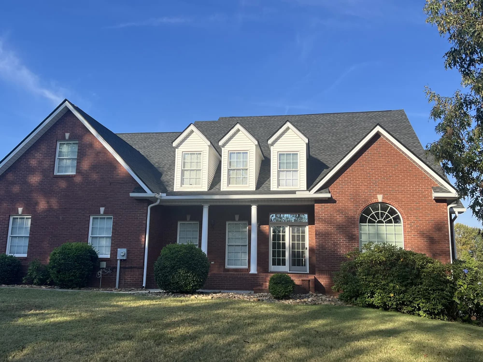Two-story brick home with a dark gray architectural shingle roof and three dormers, from our Knoxville office's job photos