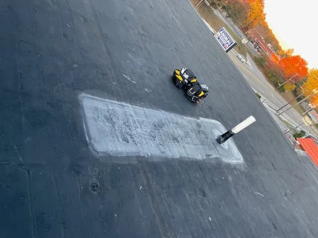 Overhead view of a black EPDM roof with a rectangular membrane patch around a pipe penetration